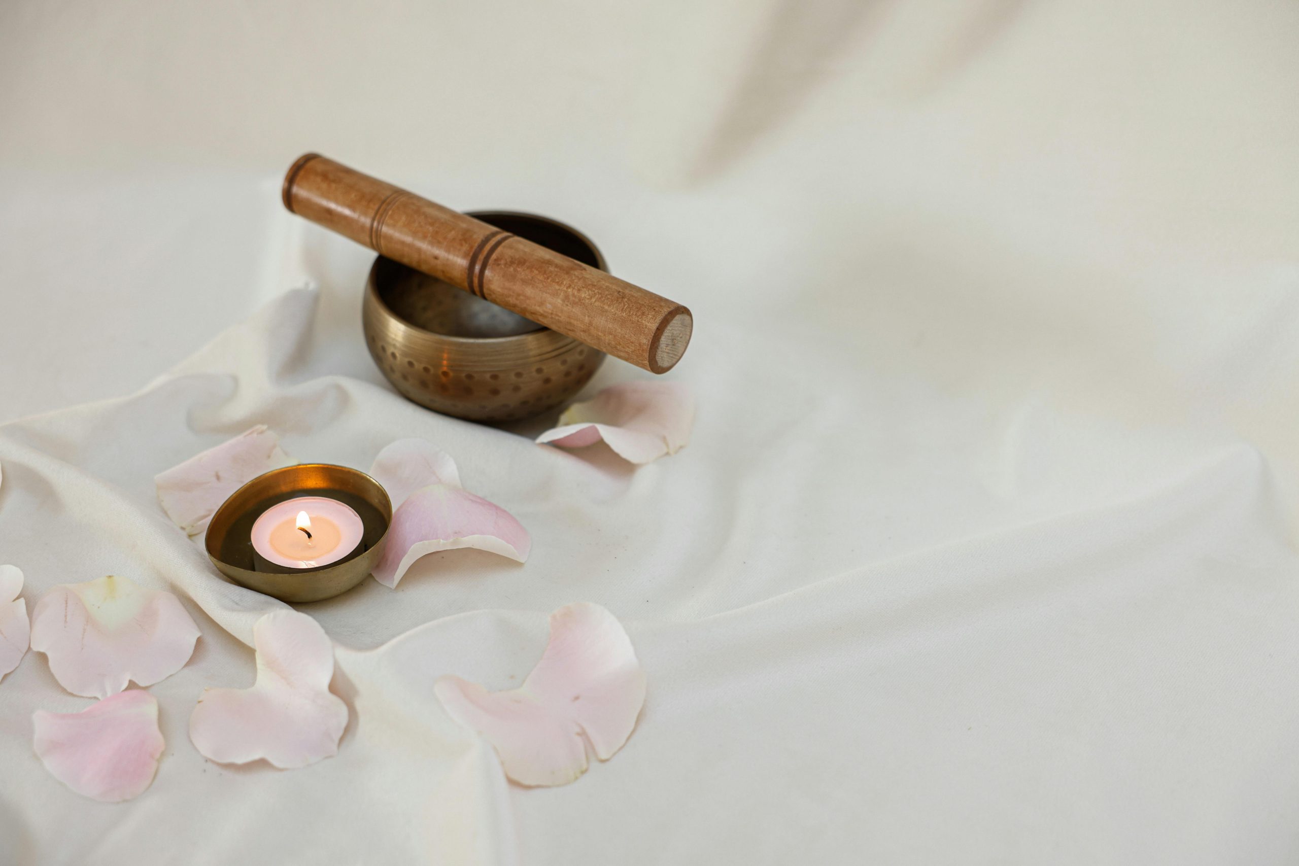 Elegant still life featuring a Tibetan singing bowl, lighted candle, and soft rose petals for relaxation.